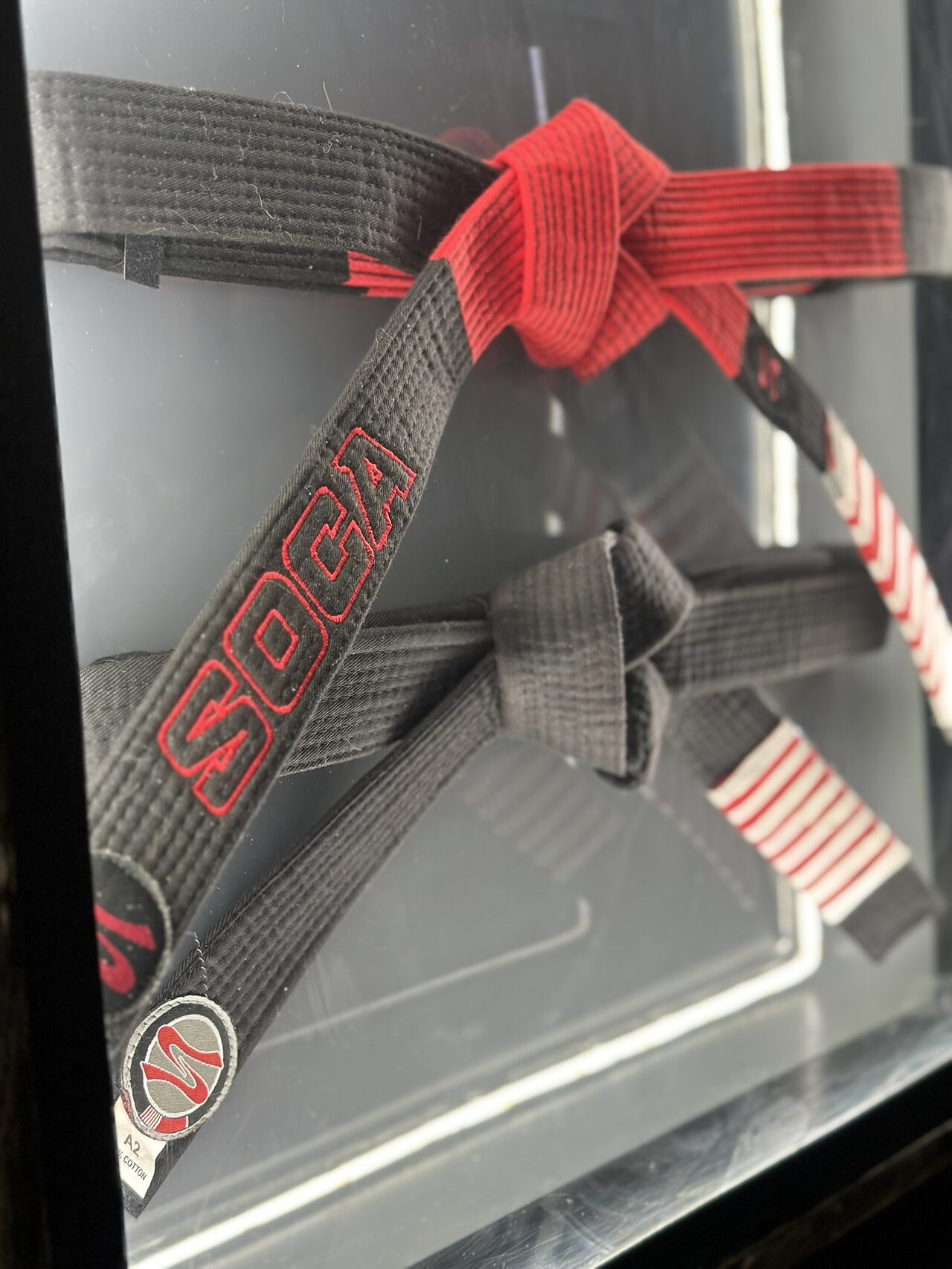 Angled close-up of the two knotted belts inside the case, with a round Soca patch and a line of white LED light along the bottom.