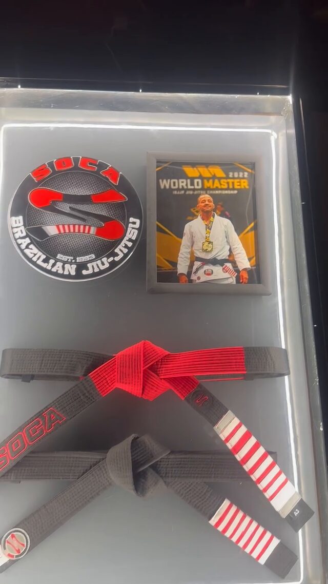 The case in a dark room, its back panel glowing white behind the logo, the framed photo and the belts.