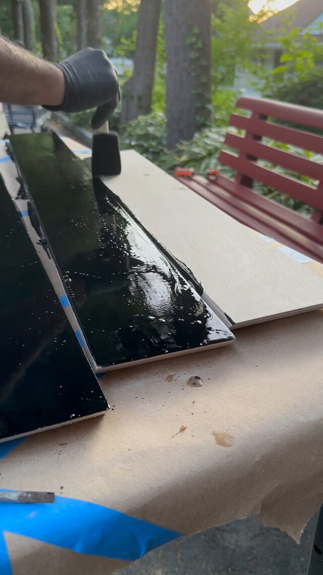 Frame boards painted gloss black, drying on a bench outdoors.