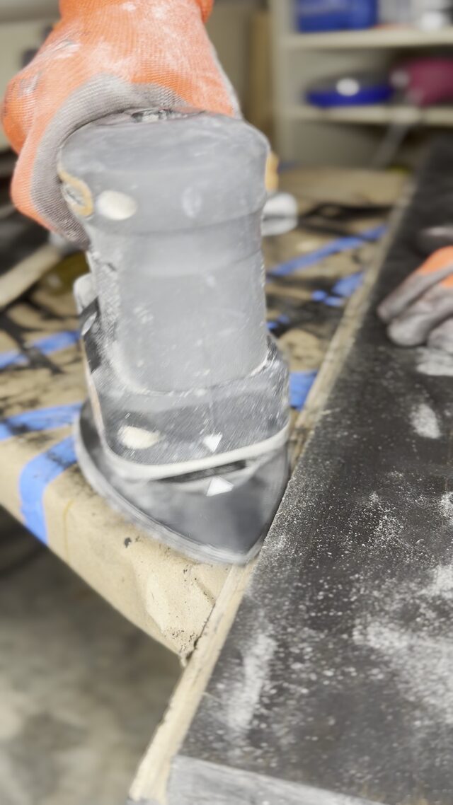 A trim router running along a black frame board clamped to the bench.