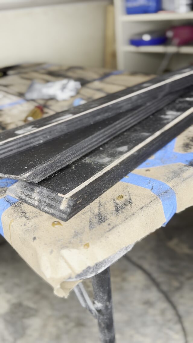 A stack of grooved black frame lengths on the bench.