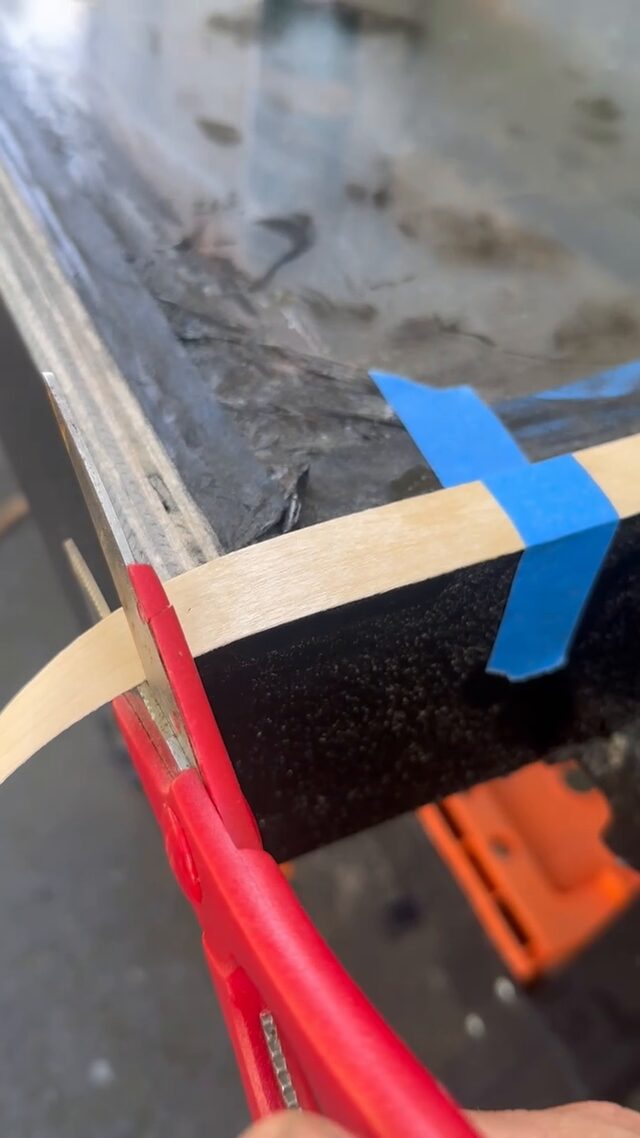 Scissors trimming the veneer banding at a taped corner of the frame.
