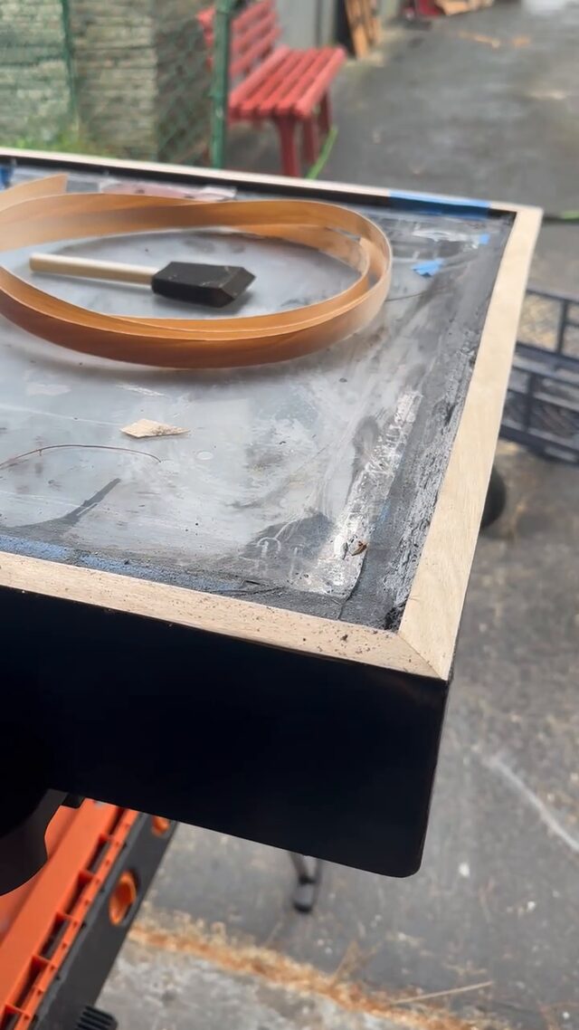 The case on a stand outdoors, its edge banded, with the banding roll and a foam brush on top.
