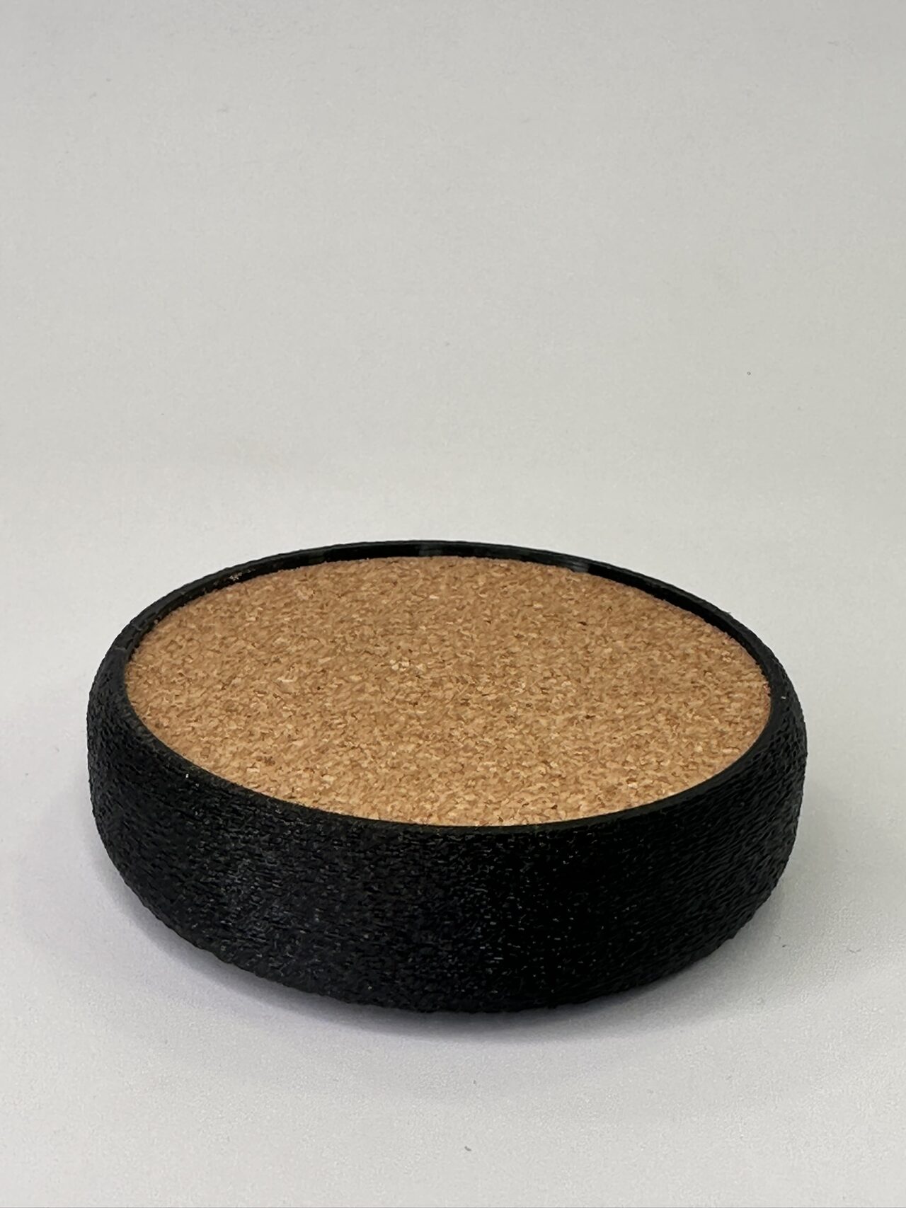 Black printed coaster with a cork top seen from a low angle on white