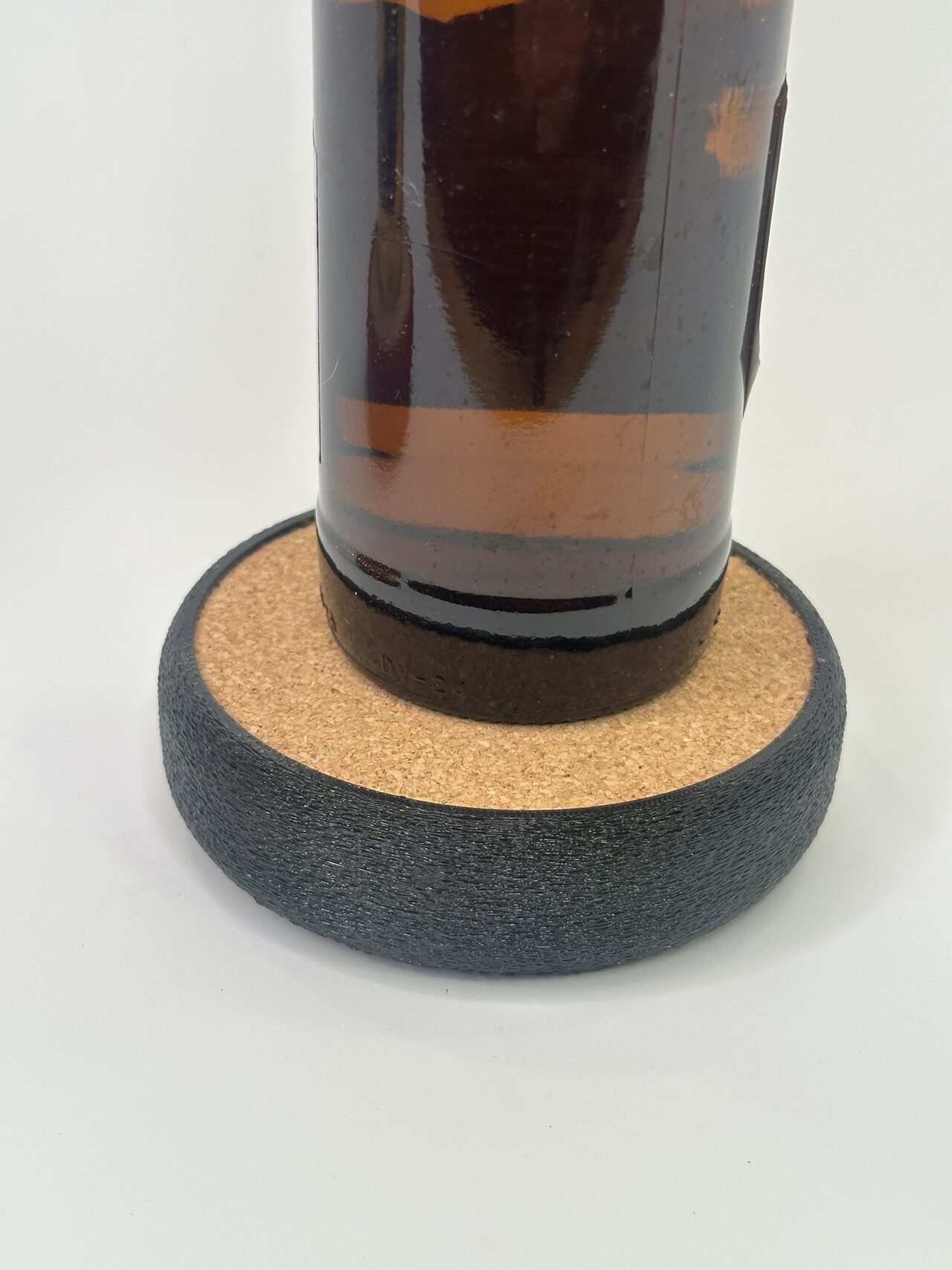 Close view of a brown bottle base resting on the cork of a black textured coaster