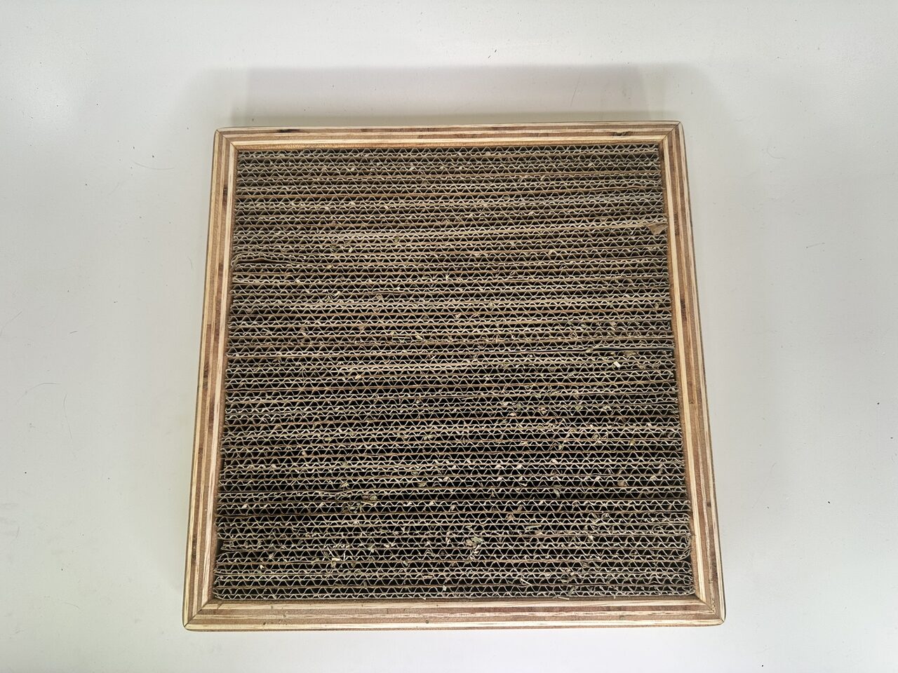 Top-down view of the scratching surface: rows of corrugated cardboard strips on edge inside the plywood frame.