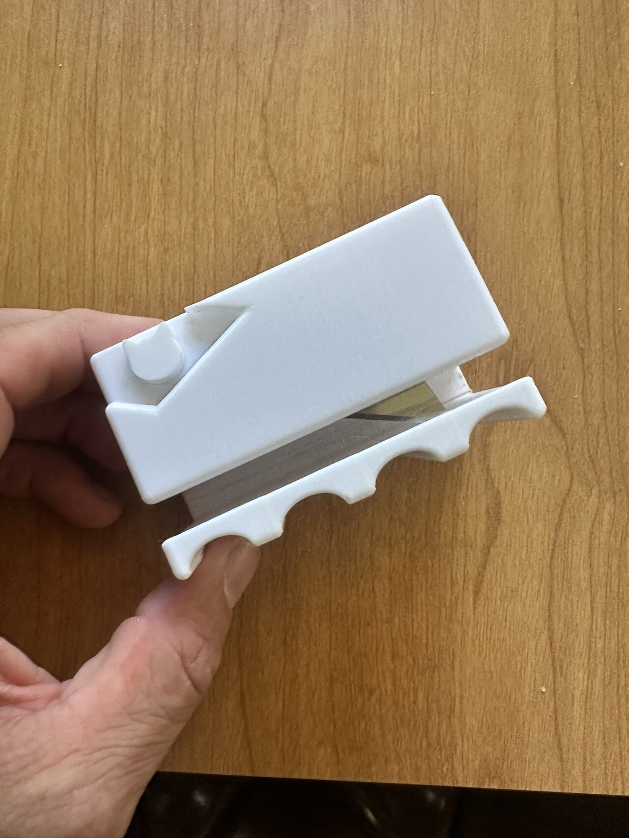 A hand holding a small white 3D-printed cutting guide with an angled slot and a scalloped base.