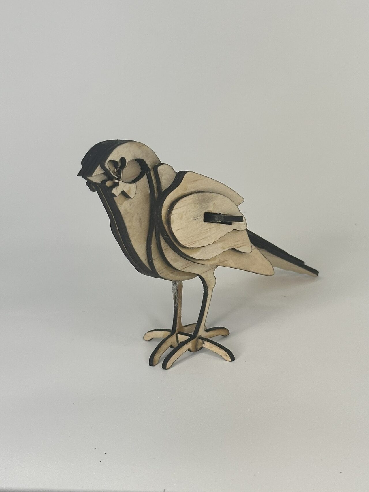 The layered wood bird seen three-quarter from the front on a pale grey backdrop, showing the stack of layers across its breast.
