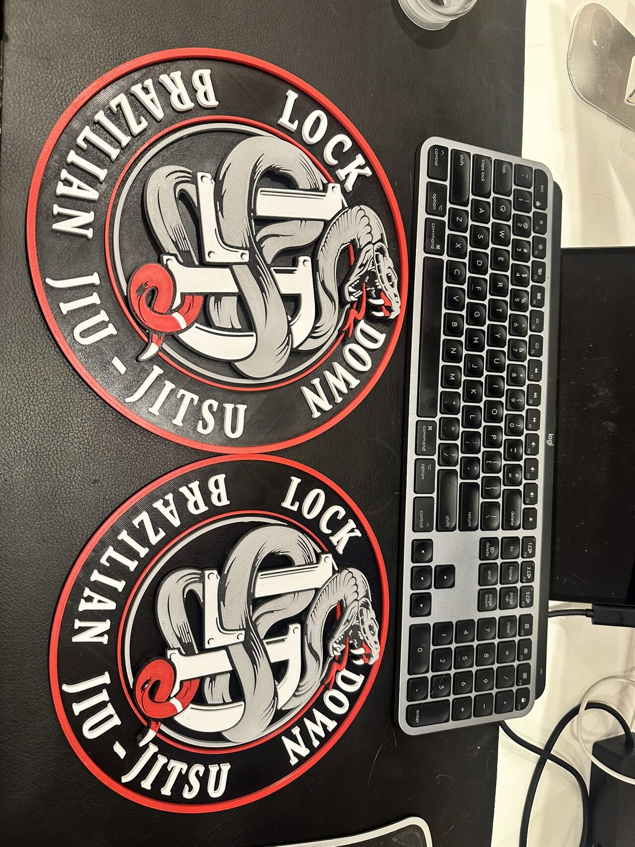 Two matching round Lock Down logo plaques side by side on a desk mat next to a keyboard.