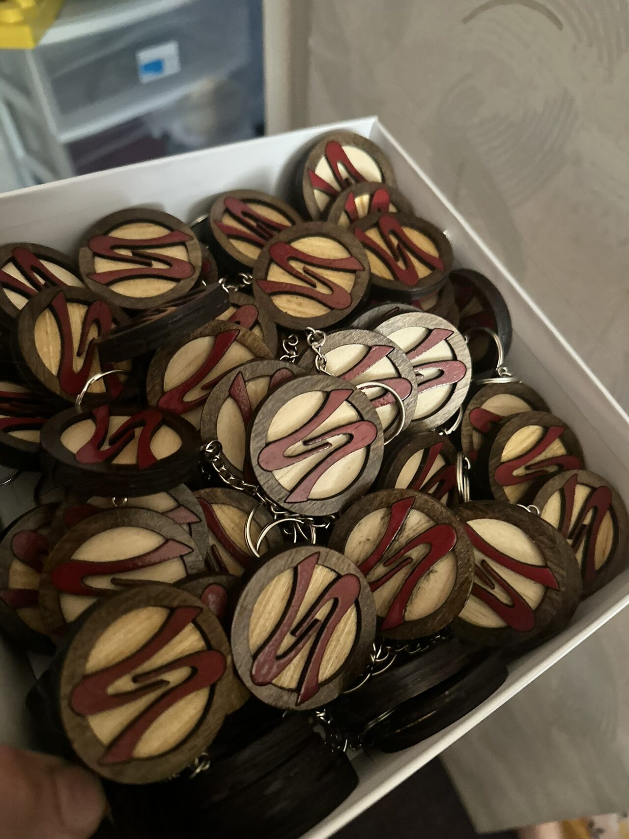 A white box filled with round wood Soca logo keychains, dark outer rings with light centres and red S shapes.