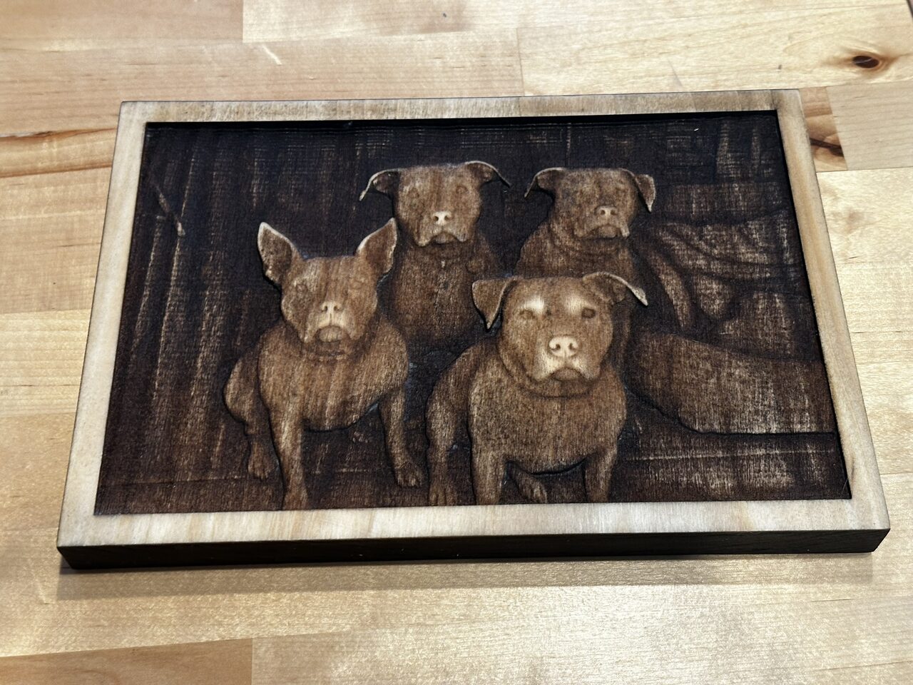 Landscape wood plaque engraved in deep relief with four dogs sitting together, no lettering.