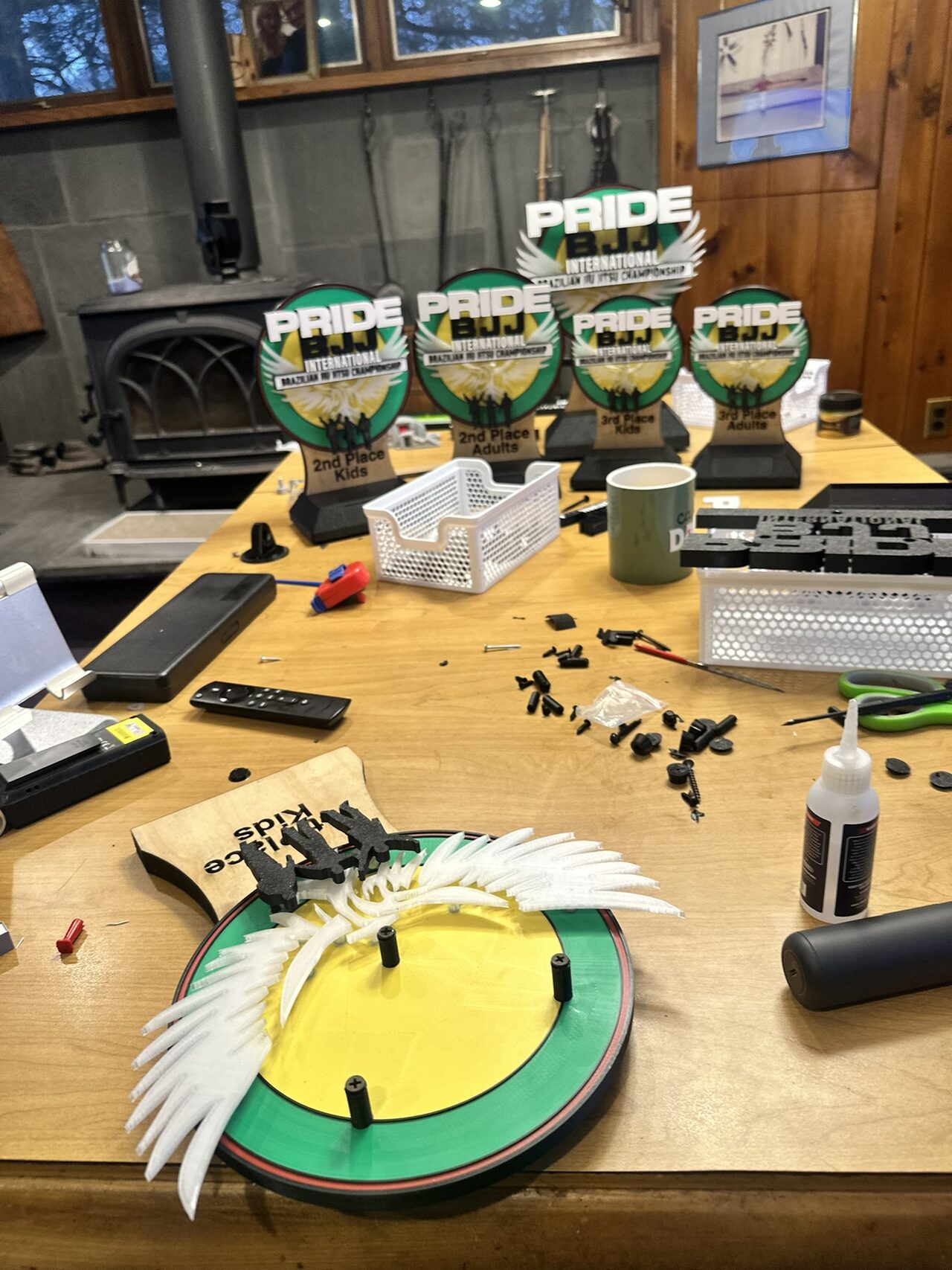 A workbench with finished trophies at the back and, in front, a green and yellow disc with white wings fitted and loose black parts around it.