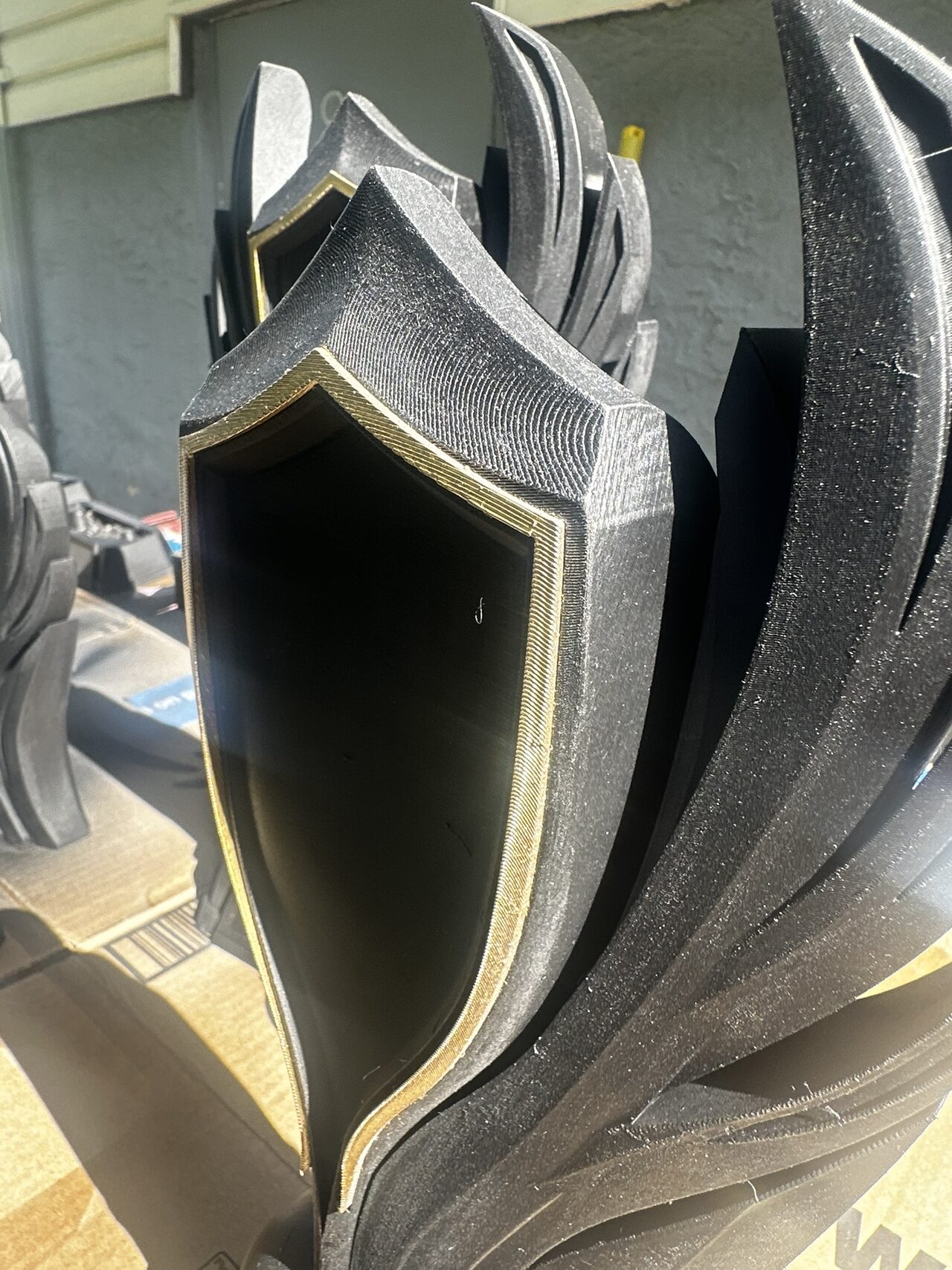 Close view of a black trophy body with an empty shield recess whose raised edge is finished in gold; print layer lines are visible.
