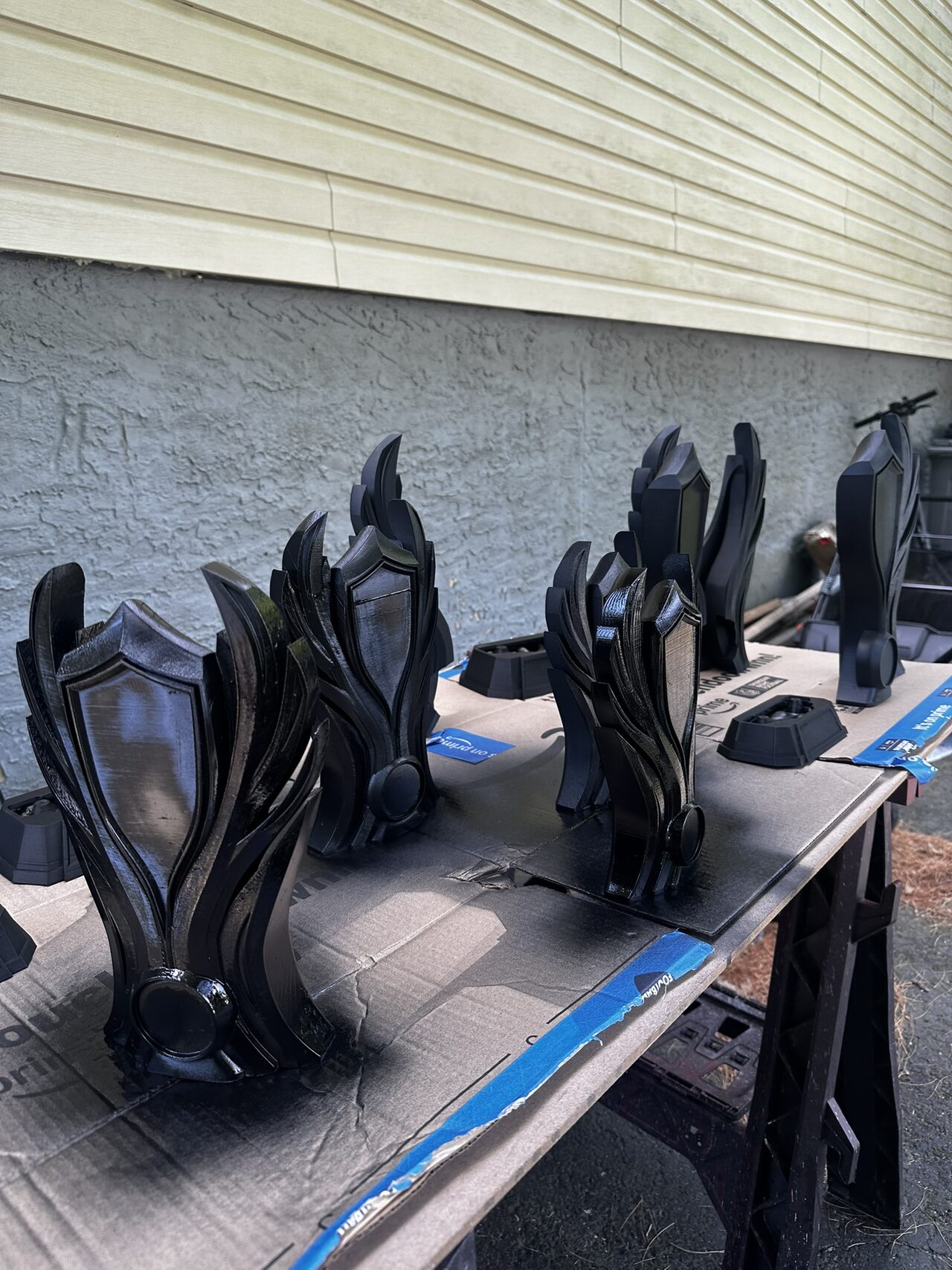 Several black trophy bodies and bases drying on a masked work table outdoors.