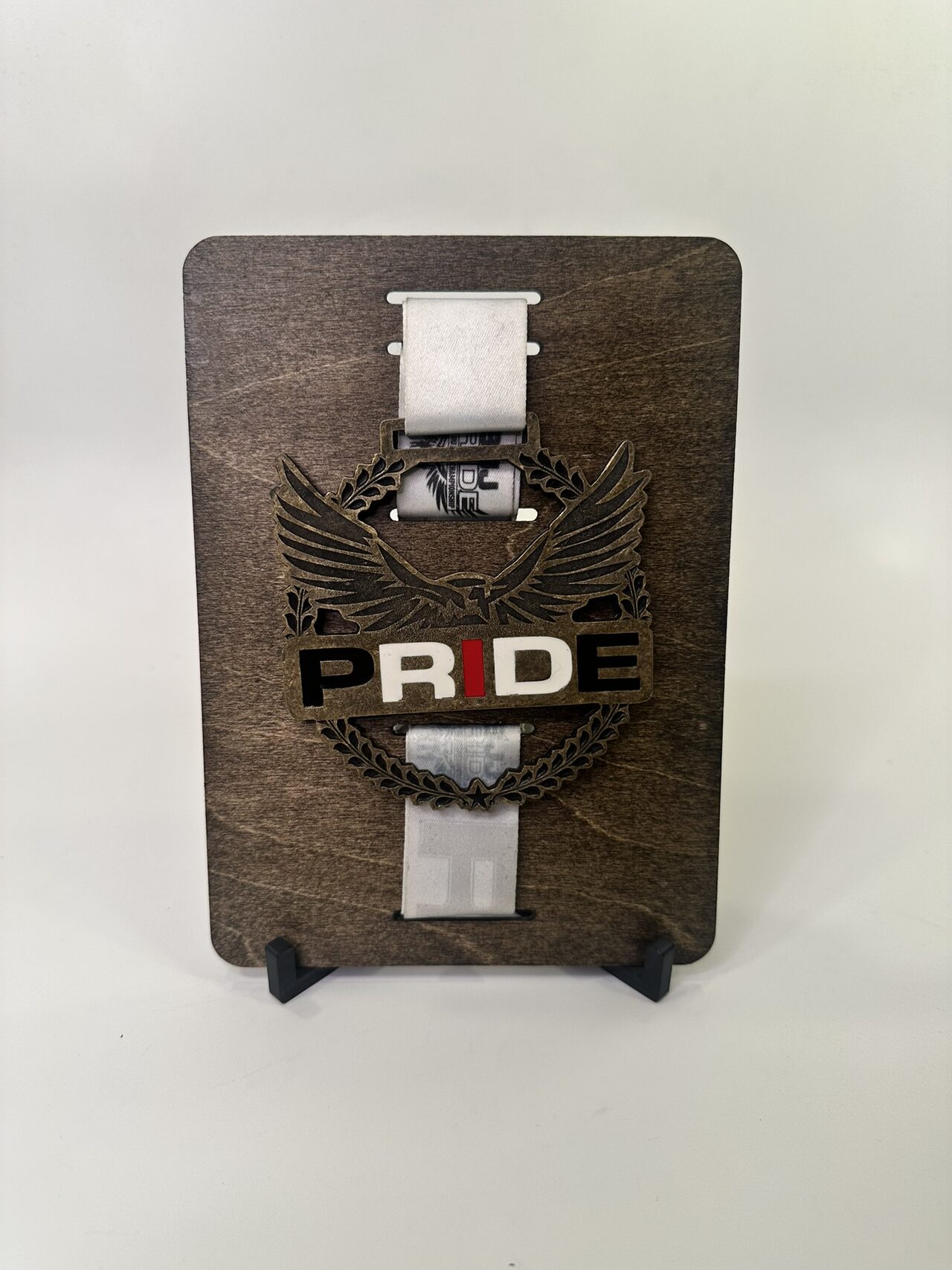 Straight-on front view of the stained wood medal board on its black stand, PRIDE eagle medal centred, white backdrop.