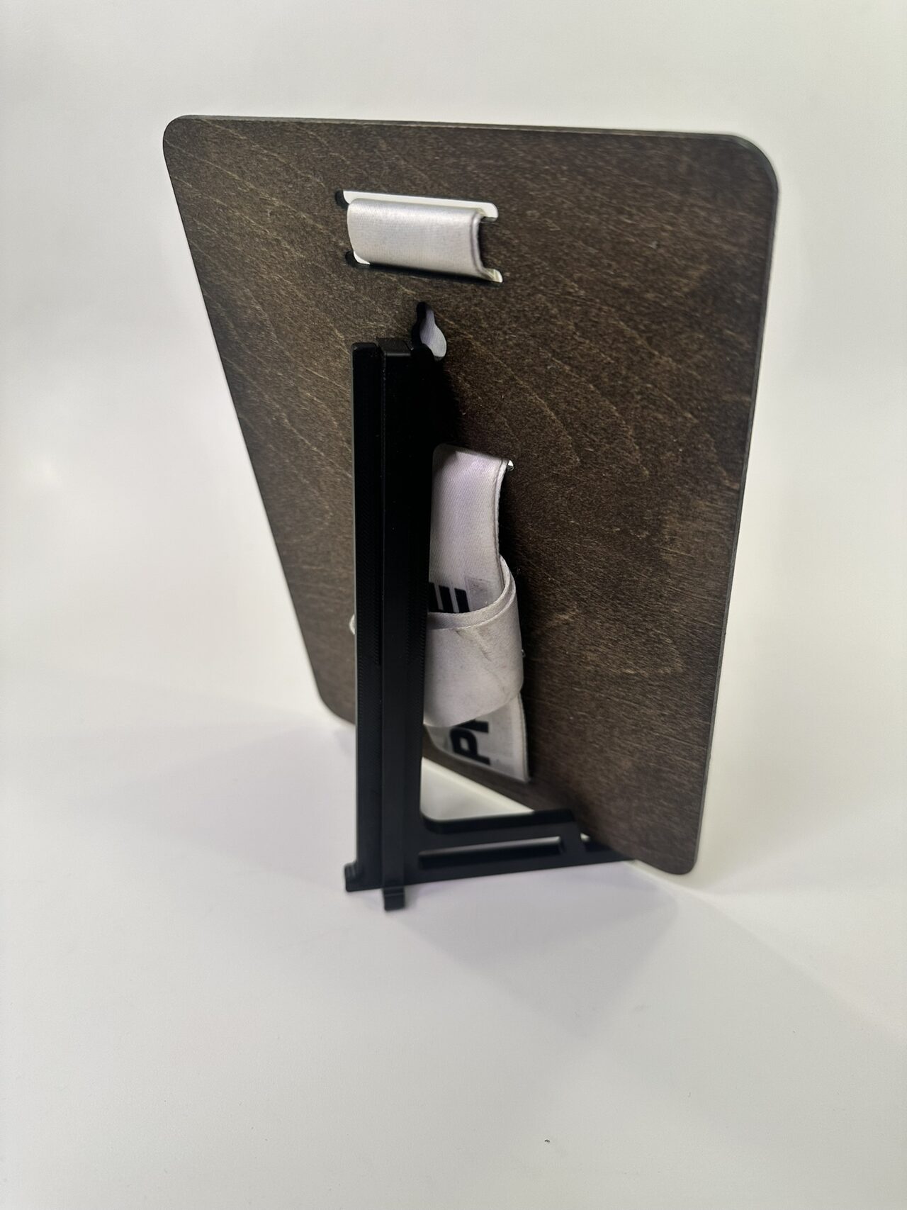 Back of the wood board on its black two-piece stand, with the folded white ribbon tucked through the slots and a keyhole cut near the top.