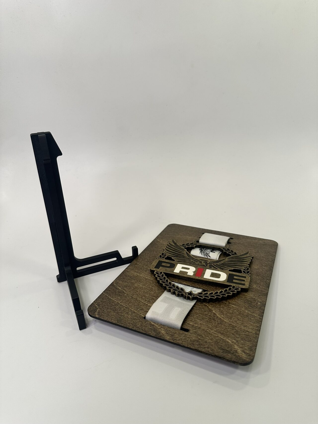The board with its medal lying flat on a white surface beside the empty black stand standing upright.
