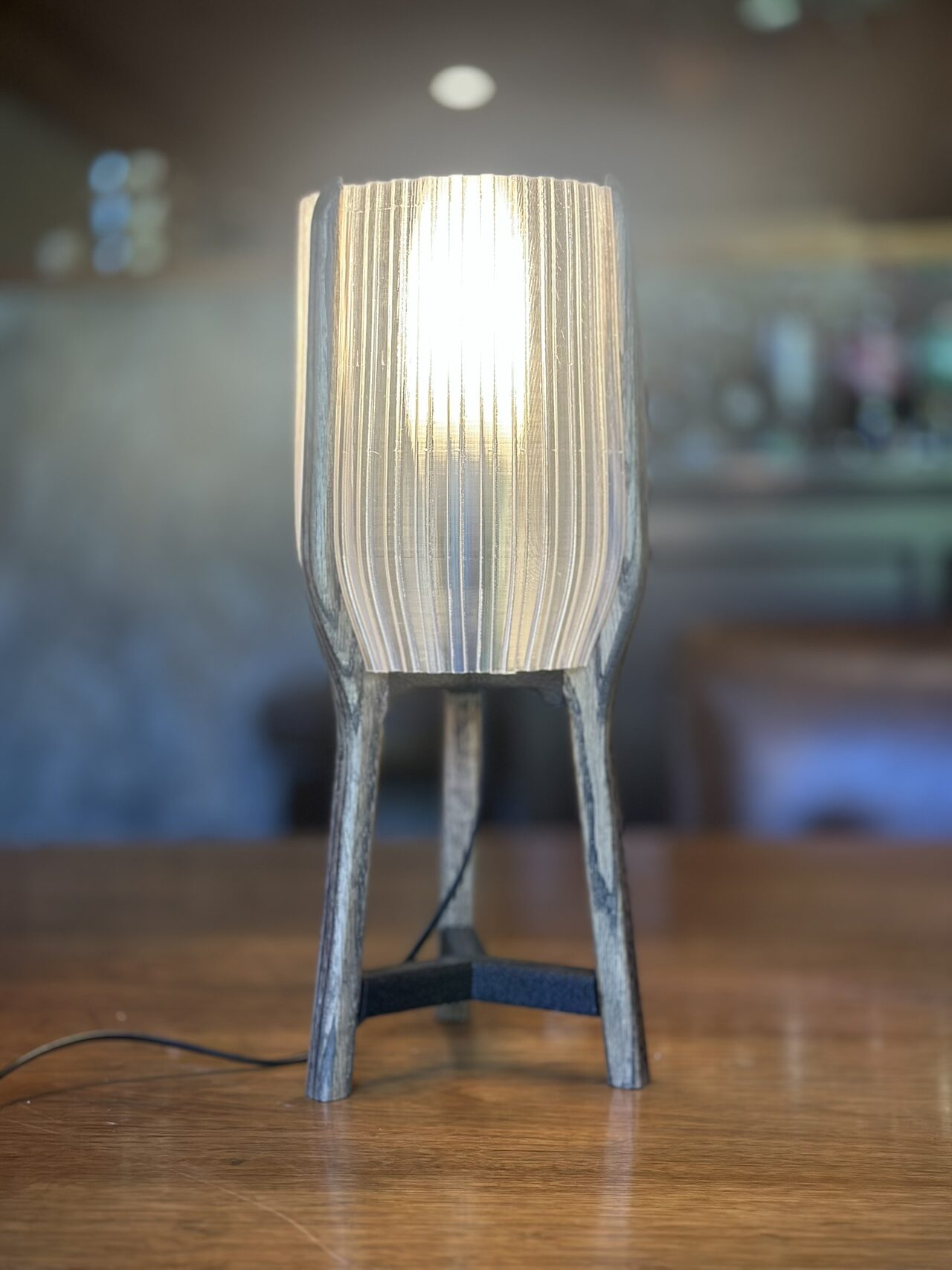 The same lamp with a white ribbed shade, switched on, alone on a wooden table