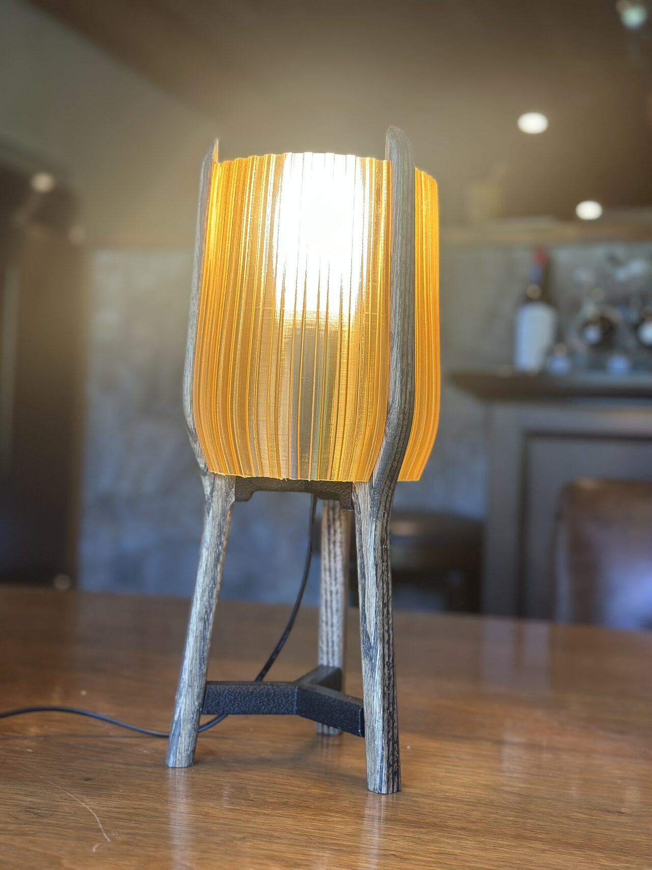 The lit amber lamp from a three-quarter angle showing the curve of a wooden leg and the depth of the shade