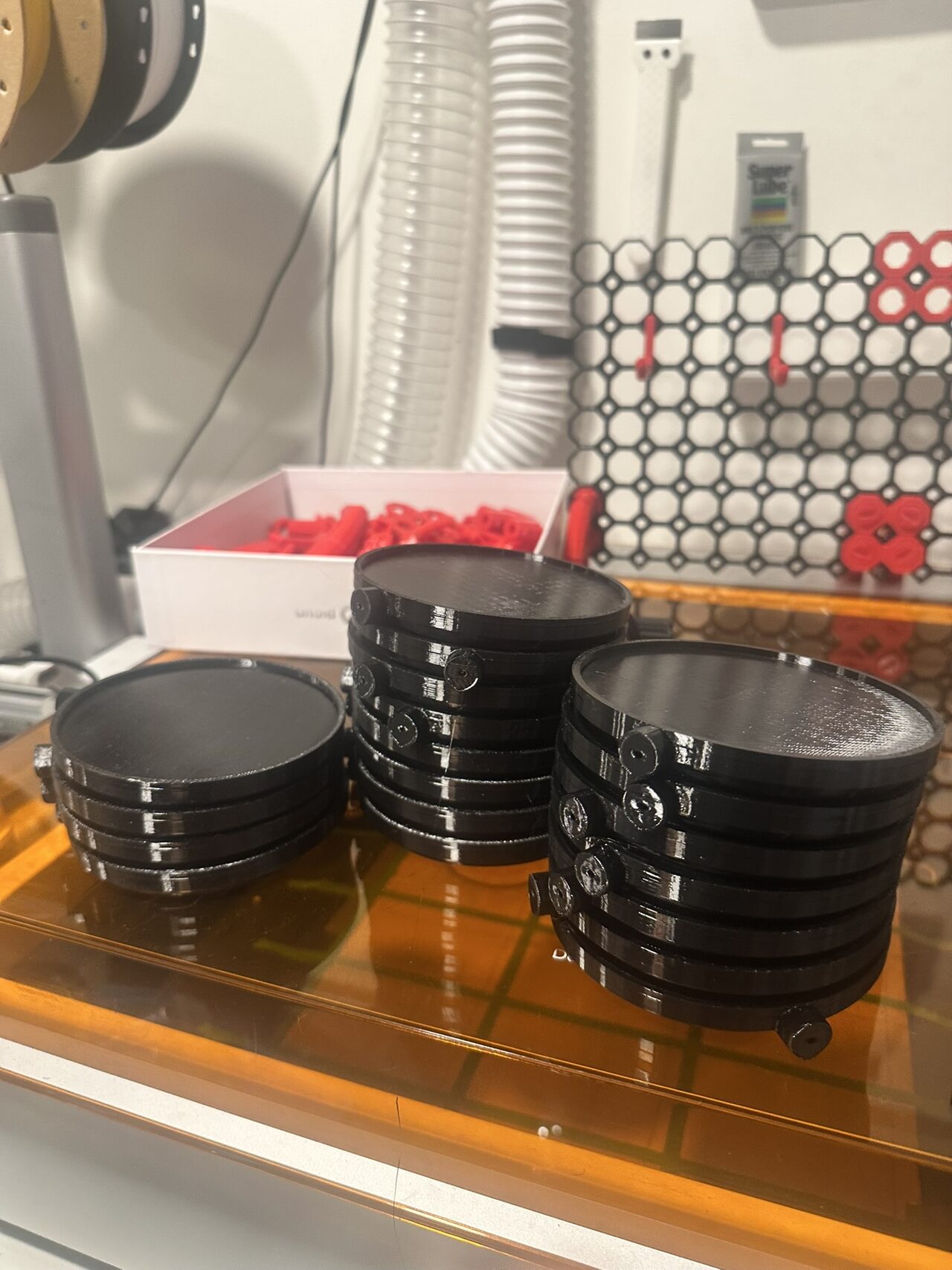 Stacks of black printed medallion bases piled on top of a machine enclosure in the shop