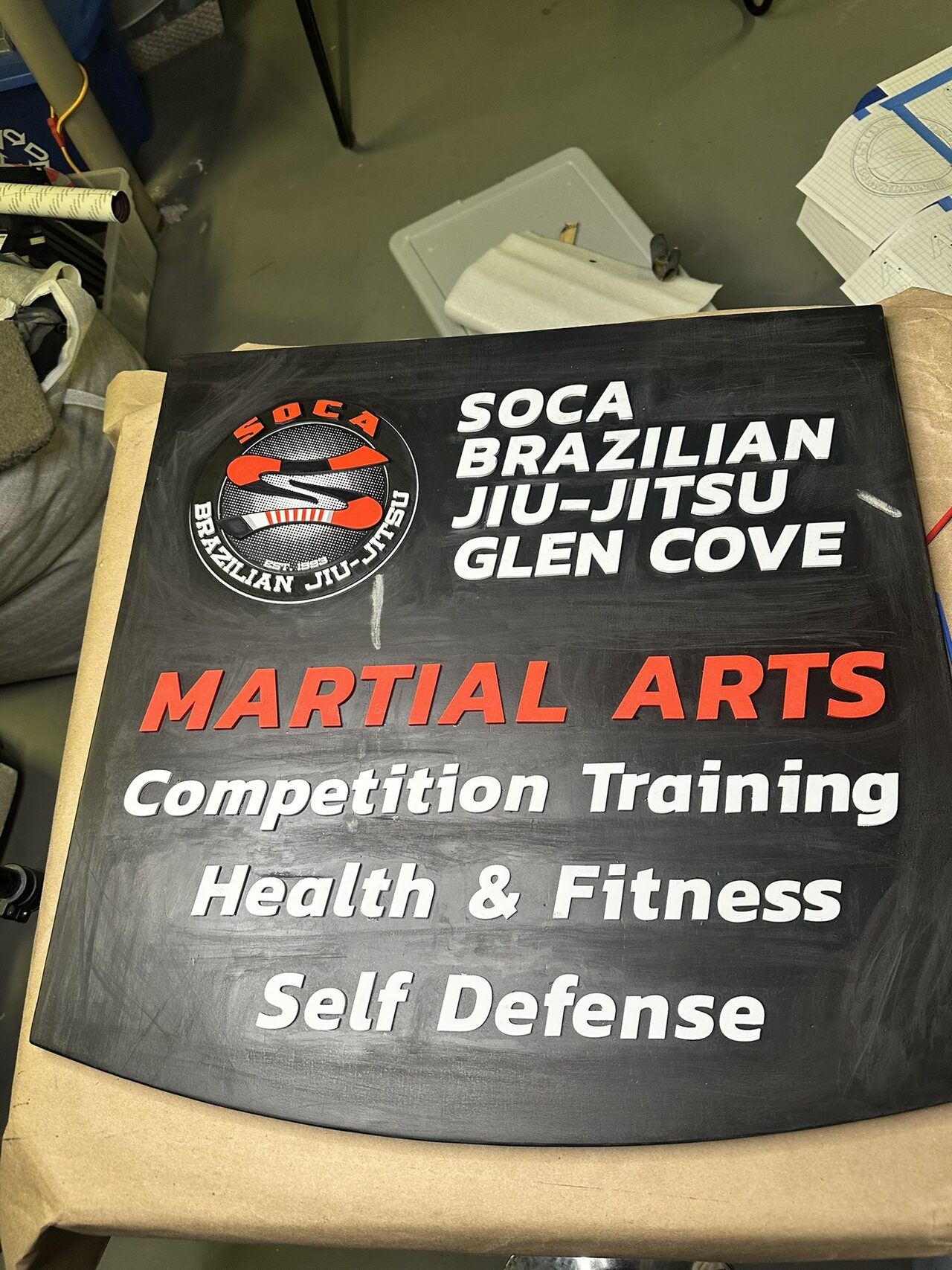 Blade sign panel lying on a workbench, with the round logo and raised white and red lettering in place.