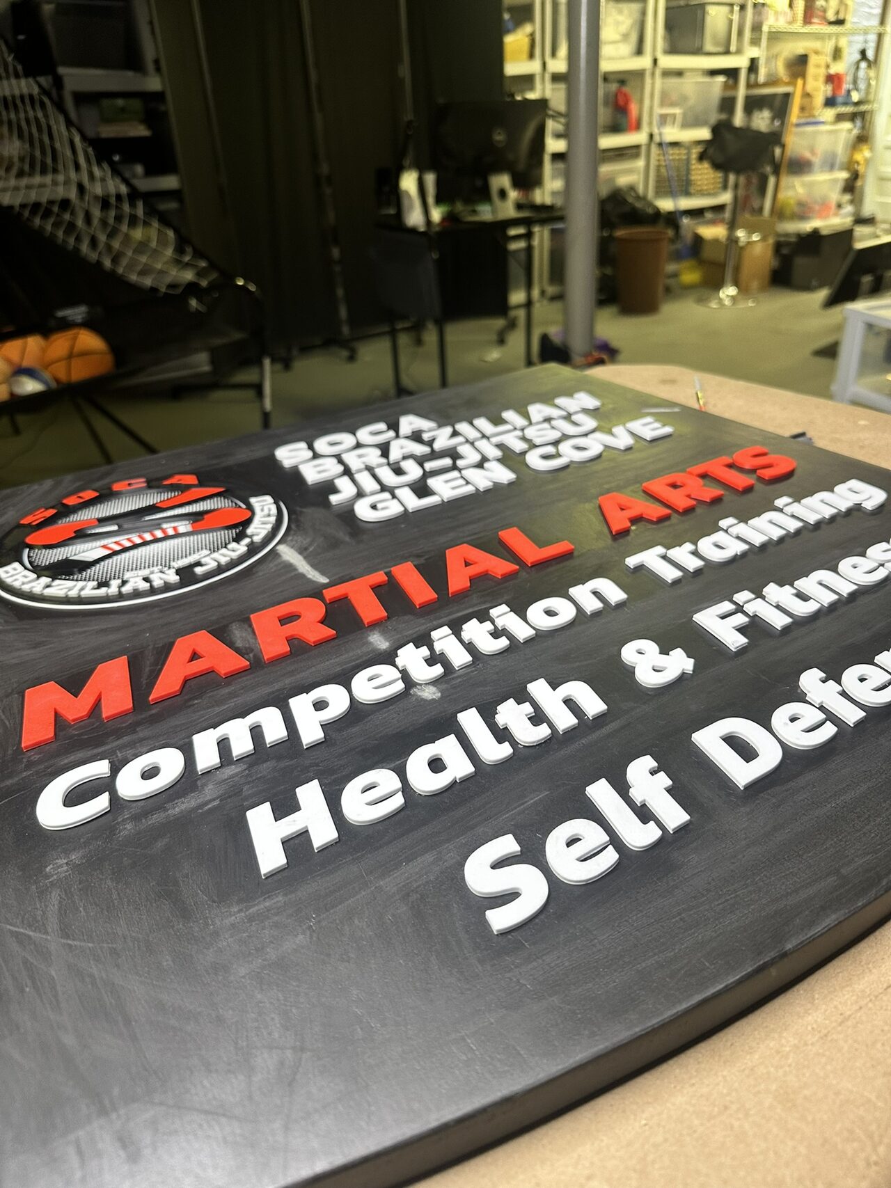 Low angle across the blade sign panel showing the raised red Martial Arts letters and white lettering standing off the black surface.