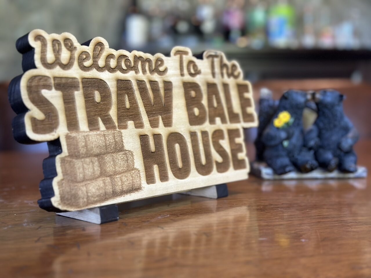 Angled close view of the sign showing the black backing layer along its left edge, with a bear figurine beside it.