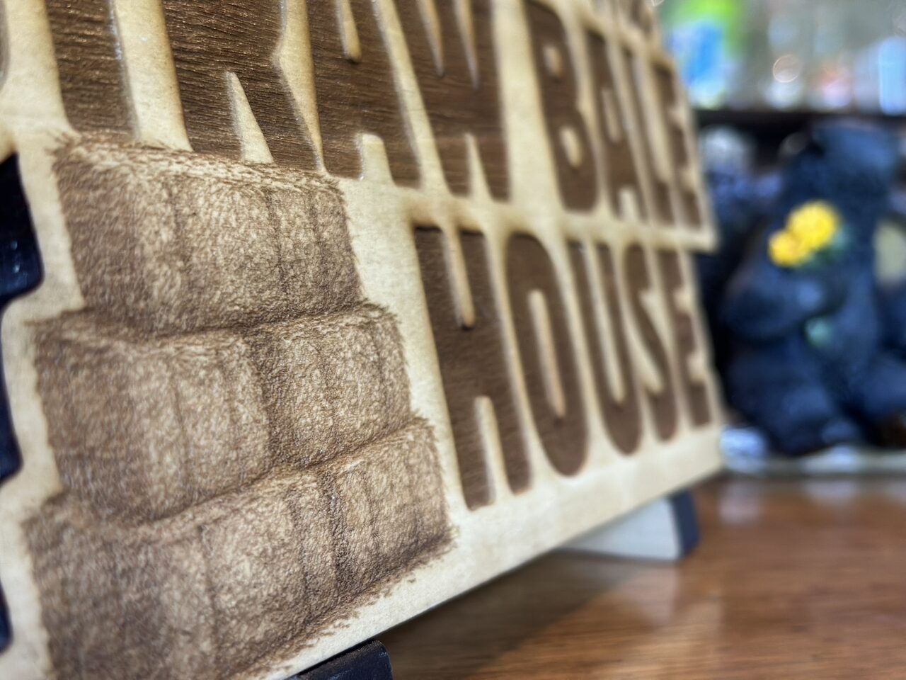 Macro view of the engraved stack of straw bales and the letters of the word HOUSE, with wood grain visible in the engraving.