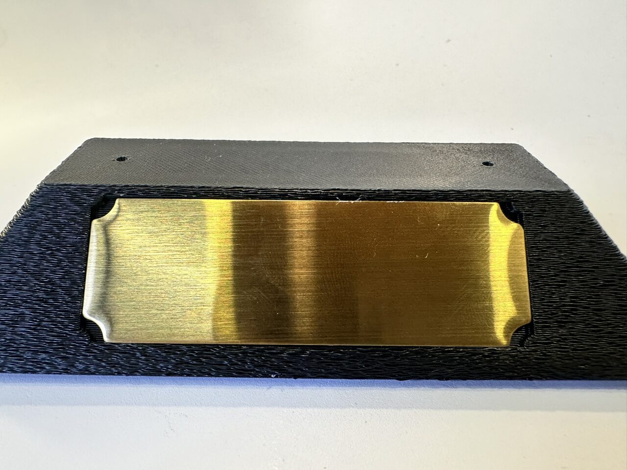 Textured black 3D-printed base with a blank brushed brass plate set into a recess on its front face.