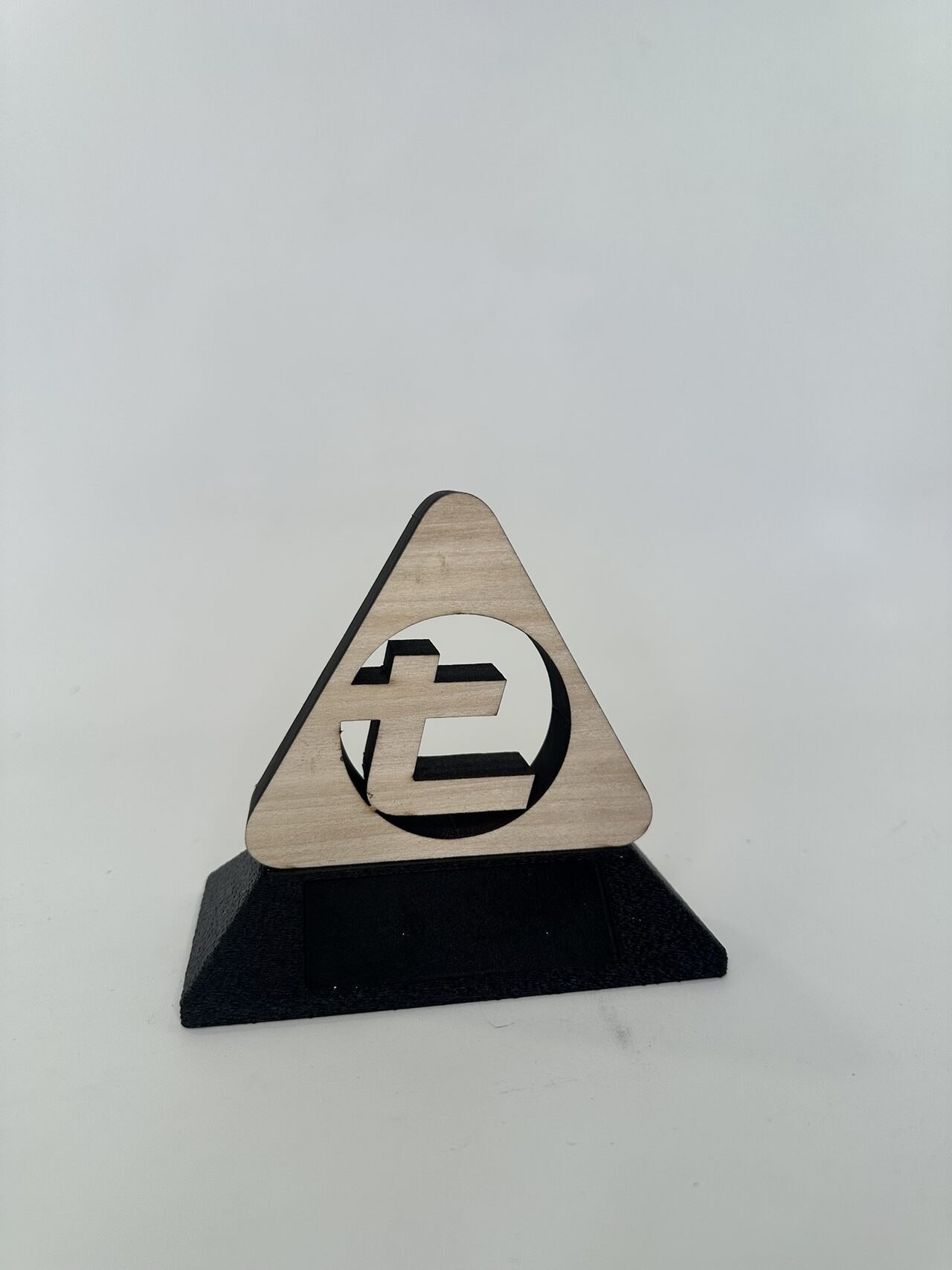 Small prototype on a white surface: a laser-cut plywood triangle with the logo cut through, standing on a black printed base.