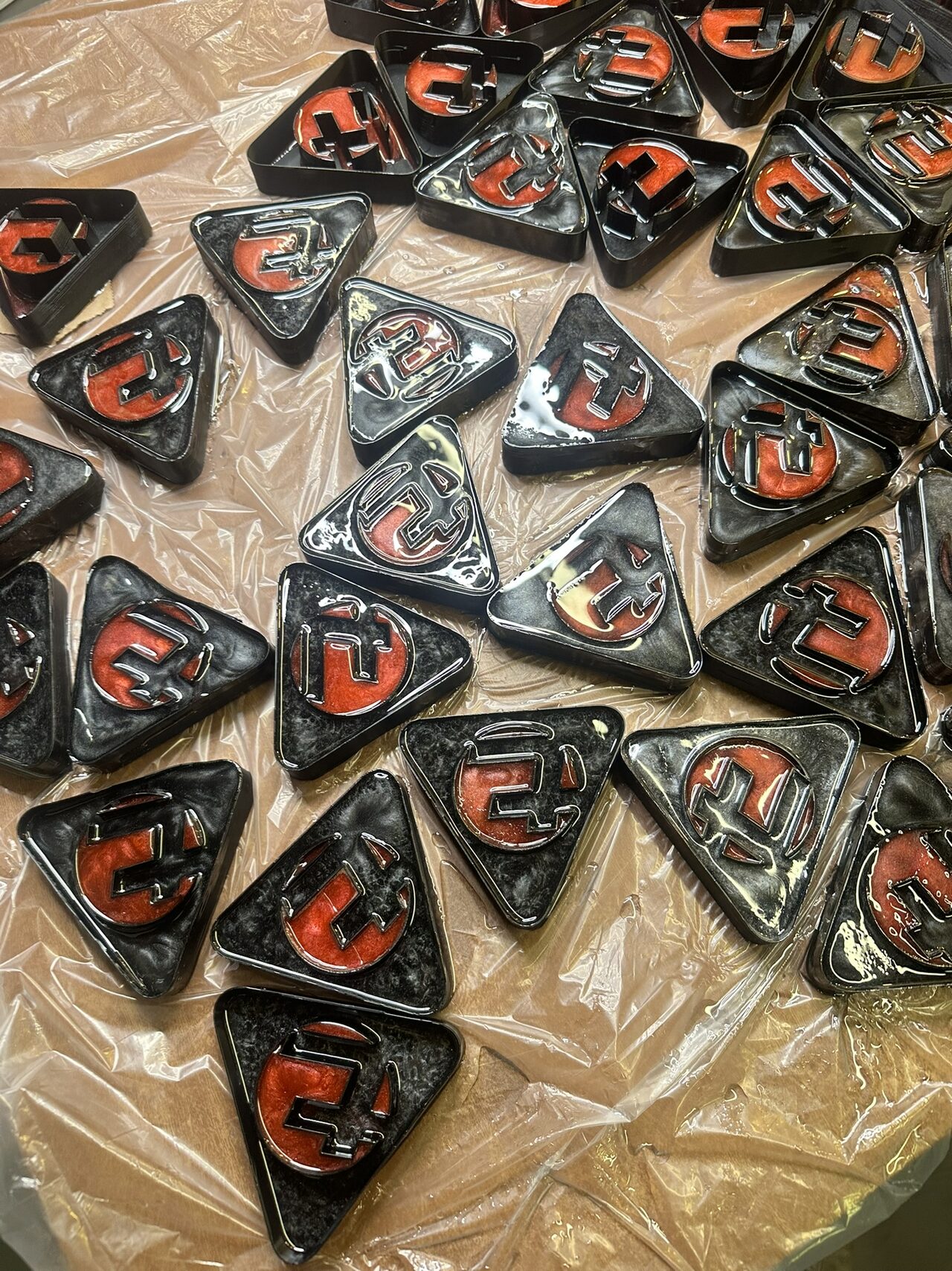 Overhead view of about twenty black triangles with red resin logos laid out on plastic sheet to cure.